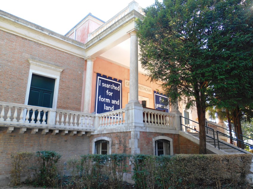 Figure 3.3: View looking south toward the British pavilion converted from an older 1897 tea pavilion in 1909 by Edwin Alfred Rickards, and decorated with the banners of the installation English Magic (2013) by Jeremy Deller. Photograph: Joel Robinson.